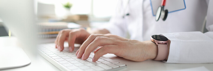 Doctor sitting at table and typing on computer keyboard closeup
