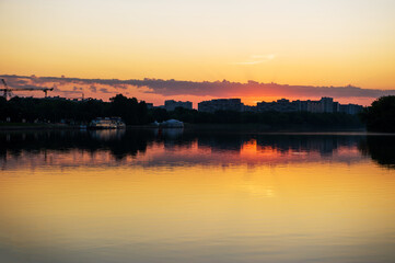 Summer sunset on the river bank. View of the city with reflections in the water
