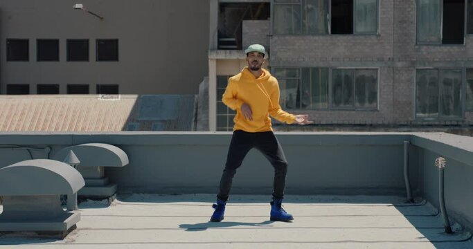 dancing man hip hop dancer performing freestyle dance moves on rooftop in city wearing yellow hoodie