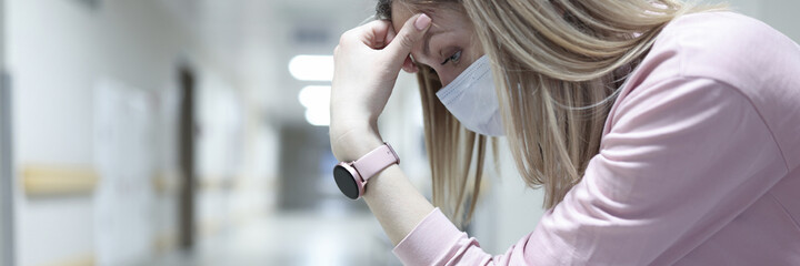 Sad woman in medical protective mask sitting in corridor of clinic