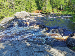 View of the bubbling waterfall with brown water on the Tokhmayoki River in Karelia from the ecological trail