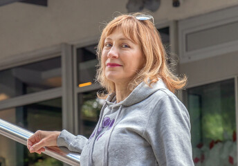 female portrait to the waist beautiful woman 50 years old with blond hair, in a sweatshirt, stands,...