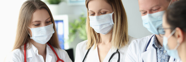 Group of doctors in protective medical masks standing with documents in their hands in clinic