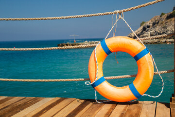Orange lifebuoy is tied with a rope to a fence on a wooden pier. Sea background