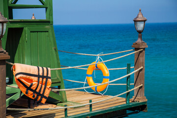 Rescue tower with lifebuoy and life jacket on a wooden pier. Sea background