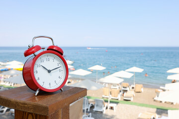 Red alarm clock standing on sea beach of hotel closeup