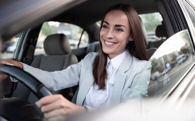 Obraz na płótnie Canvas Beautiful happy successful businesswoman is driving a new modern car in good mood. Portrait cute female driver steering car with safety belt