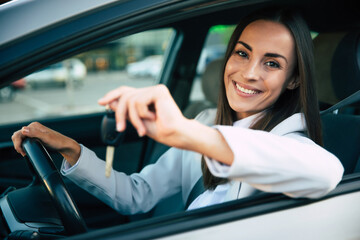 Smiling gorgeous young business woman holds the key in hand from her new car while testing this...