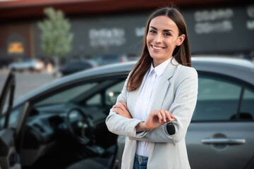 Smiling gorgeous young business woman holds the key in hand from her new car while testing this purchase - obrazy, fototapety, plakaty
