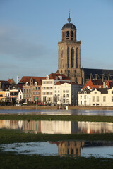 Fototapeta na wymiar The facades of beautiful old buildings and the tower of the Great Church in the city of Deventer, The Netherlands, with reflection in the river IJssel