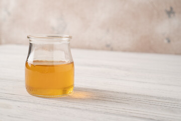 The portion of maple syrup in the small jar on a white wooden table. A portion of maple syrup