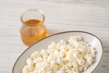 White cottage cheese with the sweet honey portion on a wooden table. Healthy breakfast of fresh cottage cheese