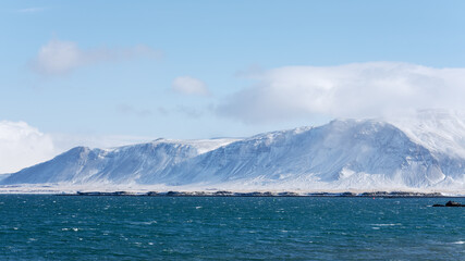 Cold day in Iceland, mt. Esja with snowy slopes and wind hitting the waves of the sea.
