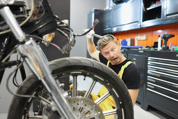 Surprised male repairman scratching his head with spanner and looking at motorcycle