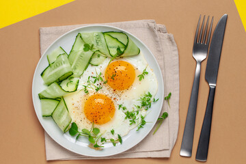 Fried eggs, cucumber and radish micrograins and cress salad in a plate on the table. Top View.