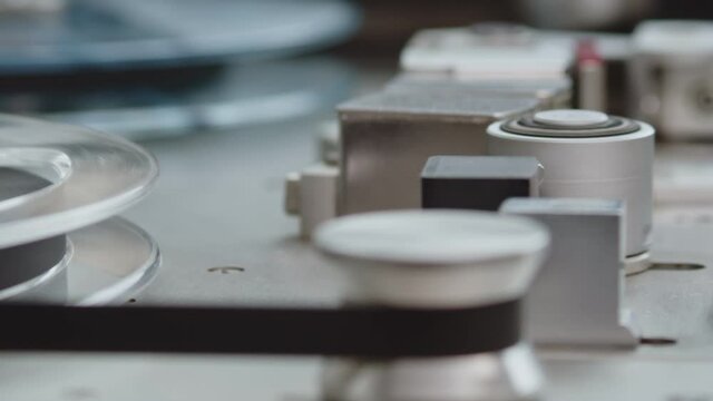 Close up of tape rolling in Nagra old professional tape recorder. Camera slide movement from flangers to magnetic head.