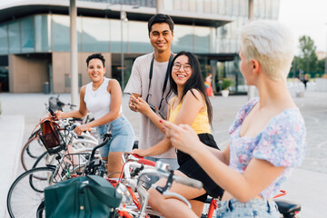 Group of multiethnic friends outdoors riding bicycles using smartphone having fun together