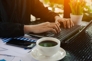 Hands of a man working on a laptop with hot coffee in the morning.