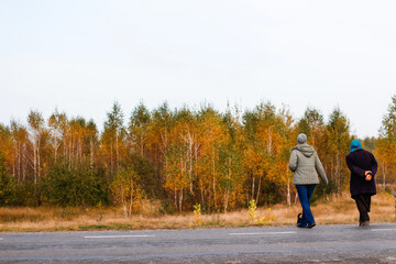 Obraz premium Defocus rear view of two woman on a walk in autumn nature cross the road. Two women walking along the road in the autumn forest. Back view. Out of focus