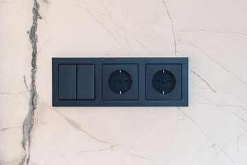 New black switch and socket on the marble wall. Kitchen background.