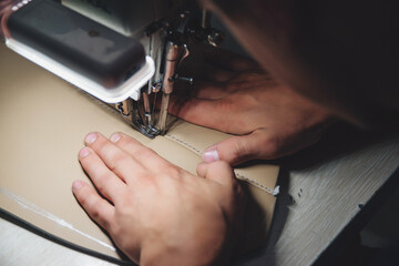 Worker sewing leather product on the sewing machine. Leather worker workshop.