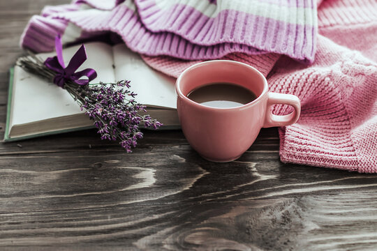 A cup of coffee on a wooden table, an open book and a warm sweater on the background of a bouquet of lavender flowers. Still life concept. Cozy morning.