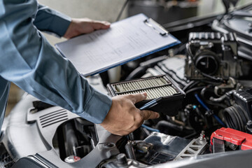 Technician hold and check the engine air filter in engine room and check list service work in the garage  : Car service concept