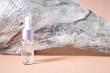 Glass dropper bottle with transparent liquid and natural wood on a beige background. Side view, place for text.