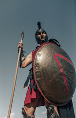 Ancient Spartan warrior in battle dress stands with shield and spear.