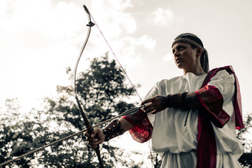 Ancient greek woman archer aims and shoots from bow on meadow.