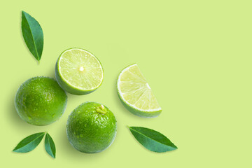 Lime fruits with leaf and cut in half slice isolated on green background. Top view. Flat lay. Copy space.