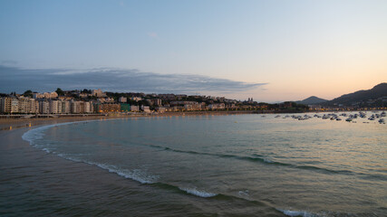 The coastline of San Sebastian, with the sea and the beach, at the sunset. Small harbour on the right, with vessels.