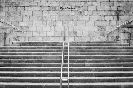 Symmetrial staircase made of stone in the historical centre of Santander, Spain. The text "Kyrie Eleison" is the title of a Greek prayer. Monochromatic.