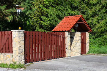 KRAKOW, POLAND - SEPTEMBER 02, 2021:  Entrance to the garden. A wooden, automatic sliding gate, a stone wall with a red roof.