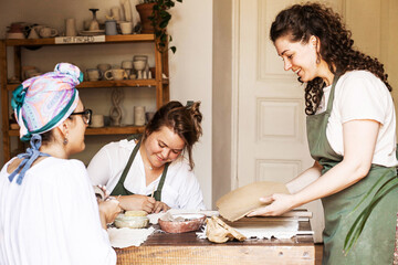 Two young women in aprons in a ceramics studio chatting among themselves and making ceramics, general plan, daylight