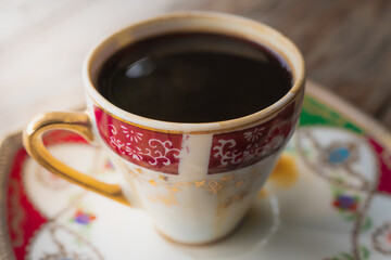 Black coffee in a porcelain victorian style cup resting on an old wooden floor gives a warm feeling.