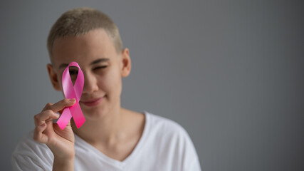 Young woman with short hair wearing a white t-shirt holding a pink ribbon as a symbol of breast...