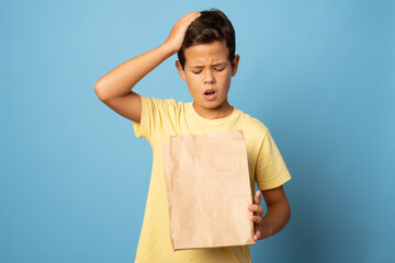 Young boy very surprised looks into the paper bag over blue background