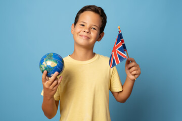 Smiling boy in casual holding globe in hands and british flag - isolated on blue