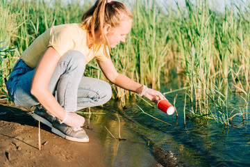 Young female volunteer satisfied with picking up trash, a plastic bottles and coffee cups, clean up...