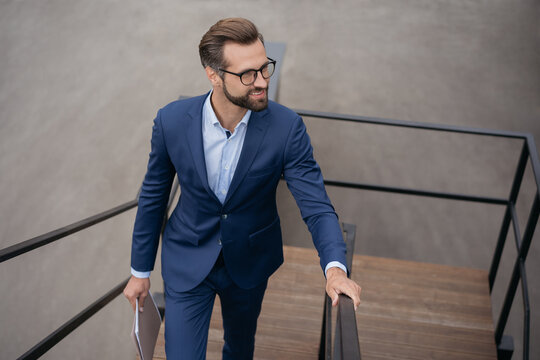 Young confident businessman holding financial documents walking up stairs looking away at copy space. Successful business, career concept