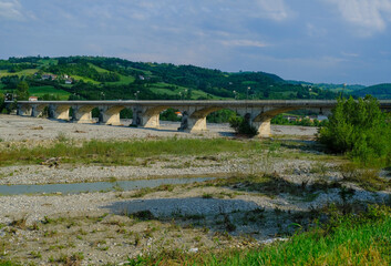Fototapeta na wymiar bridge over the mountains river Torrente Parma in summer across green hills. Langhirano, Emilia-Romagna, Italy