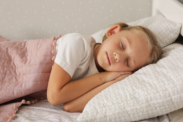 beautiful little blonde girl in a white t-shirt sleeps at home under a pink blanket