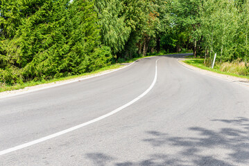 Fototapeta premium Empty Asphalt winding curve road in a green forest.Landscape with empty asphalt road through woodland in summer day.