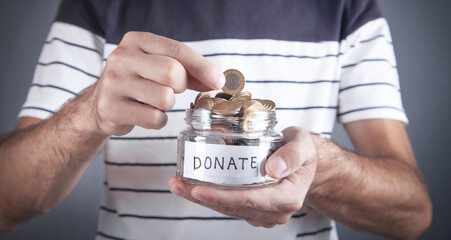 Male hand putting coin into Donation jar.
