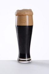 Glass of fresh and cold dark beer on a gray white light background.