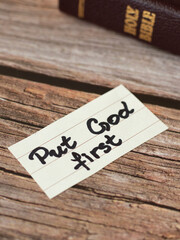 Put God Jesus Christ first. An inspiring handwritten quote (verse) with Holy Bible book on wooden background. Trust, obey, and have faith in the LORD. Christian biblical concept of obedience and love.