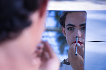 Young adult Hispanic transsexual girl doing her makeup in front of a hand mirror. Concept of...