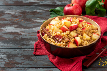 Baked bulgur with apple, honey and cinnamon in a bowl on a dark wooden background. Sweet bulgur...