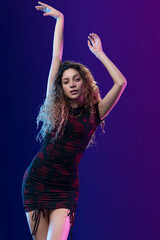 atractiva y joven mujer rizada bailando en estudio con un fondo de color azul con violeta